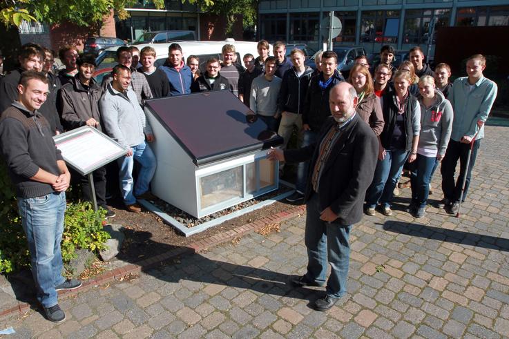 An einem Modell, das jetzt neben der Infothek auf dem Campus zu finden ist, erklärt Prof. Dr. Jan Middelberg den Studierenden die Funktionsweise von Plus-Energie und Passivhäusern. <span>Foto: Piet Meyer</span>